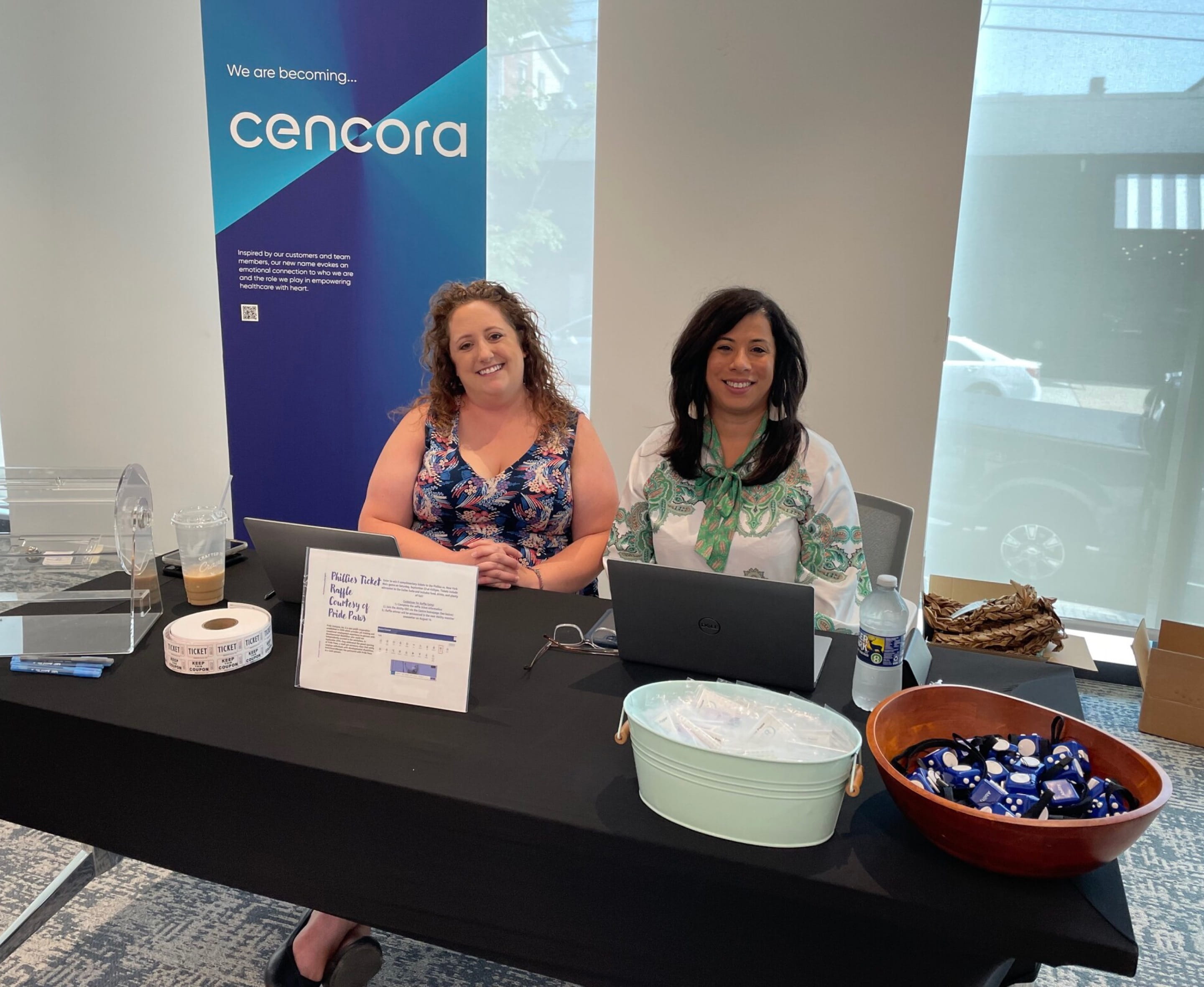Deux employés assis derrière une table dans le hall d’entrée d’un bureau distribuent des jouets à manipuler, des billets de tombola et plus encore au siège social de Cencora à Conshohocken. Elle s’inscrivait dans le cadre d’un événement célébrant l’anniversaire de la signature de l’Americans with Disabilities Act.