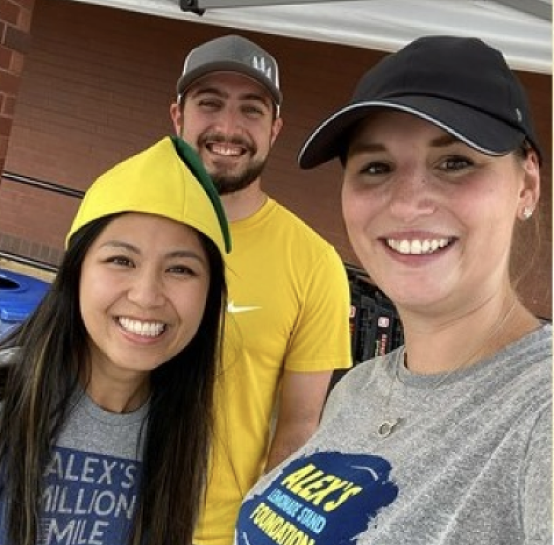 Tre volontari sorridono alla telecamera mentre indossano magliette per Alex's Lemonade Stand.
