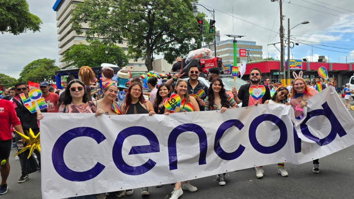 A large group of Cenora team members marching in a Pride parade while holding a big Cencora sign.