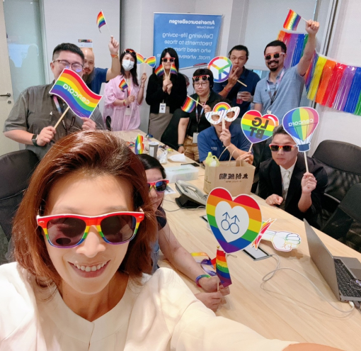 Eleven Cencora team members celebrating Pride in an office of the Cencora headquarters. They wear colorful clothes and hold up a variety of different rainbow signs.
