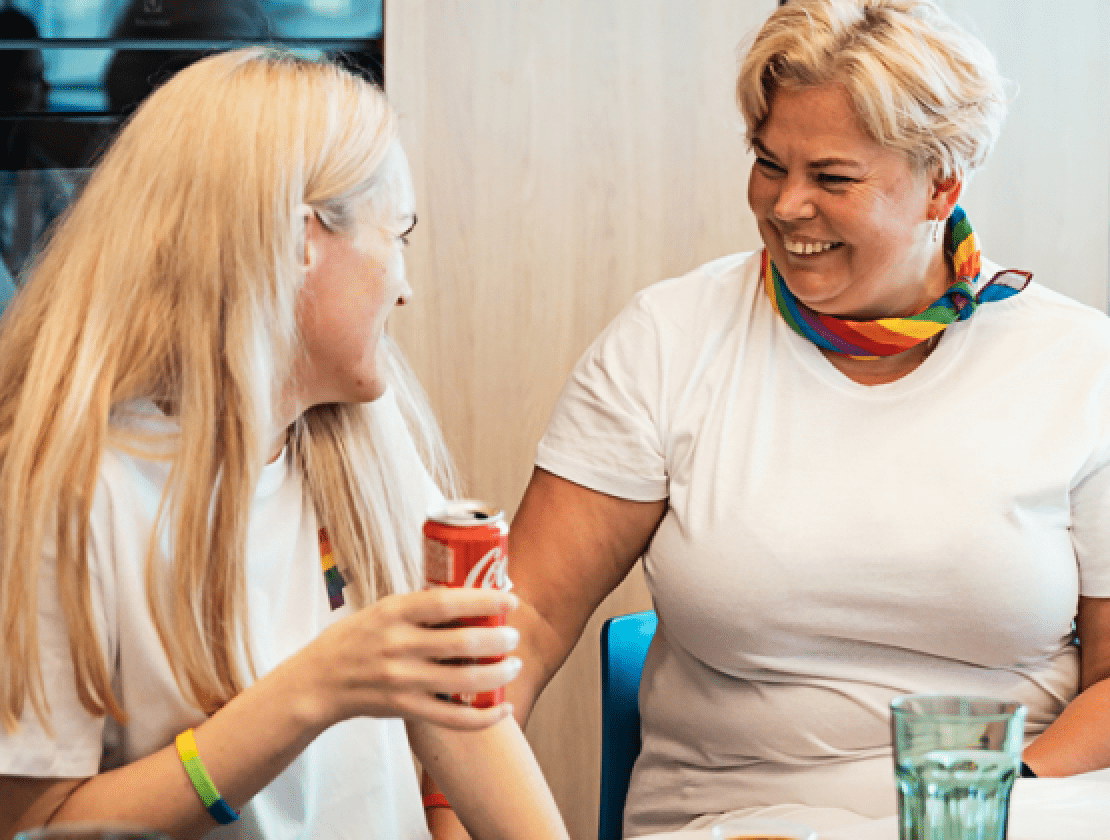 Deux femmes lors d’une manifestation de la fierté LGBTQ+ sourient et boivent des boissons.