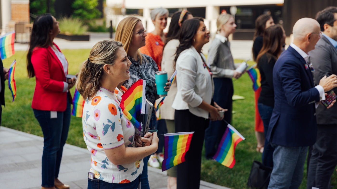 Une foule diversifiée de personnes brandit des drapeaux de la fierté arc-en-ciel lors d’un événement de la fierté LGBTQ+ en plein air.