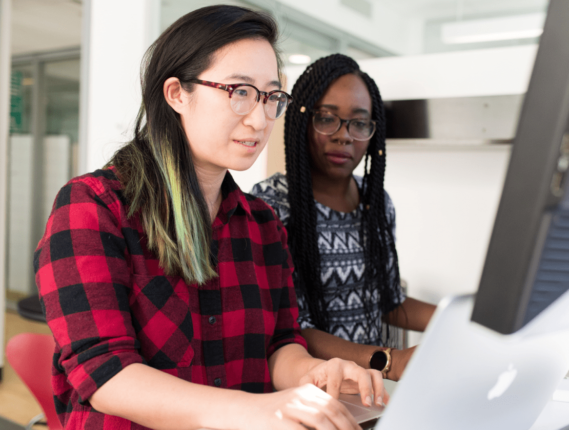 Deux jeunes femmes regardent ensemble un écran d’ordinateur.
