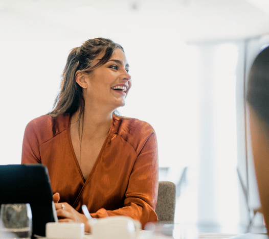 Une femme professionnelle regarde sur le côté et sourit alors qu’elle est assise à une réunion. 