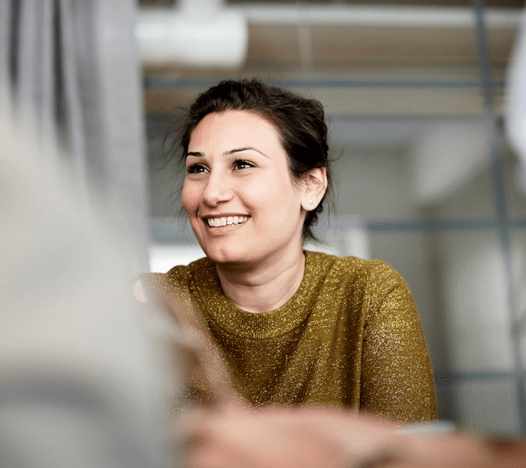 Une femme sourit alors qu’elle est assise à une réunion. 